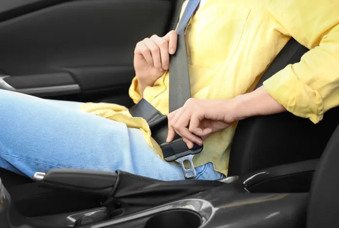 A person seated in a car drawing the seat belt across and guiding the latch plate towards the buckle.
