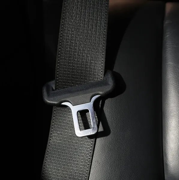 Seat belt webbing threaded through a moulded latch plate, resting against the leather trim of a vehicle seat.