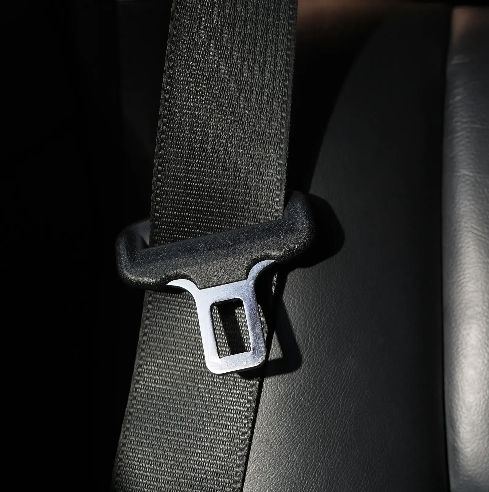 Seat belt webbing running over a vehicle seat shoulder with the metal latch plate resting against the trim.
