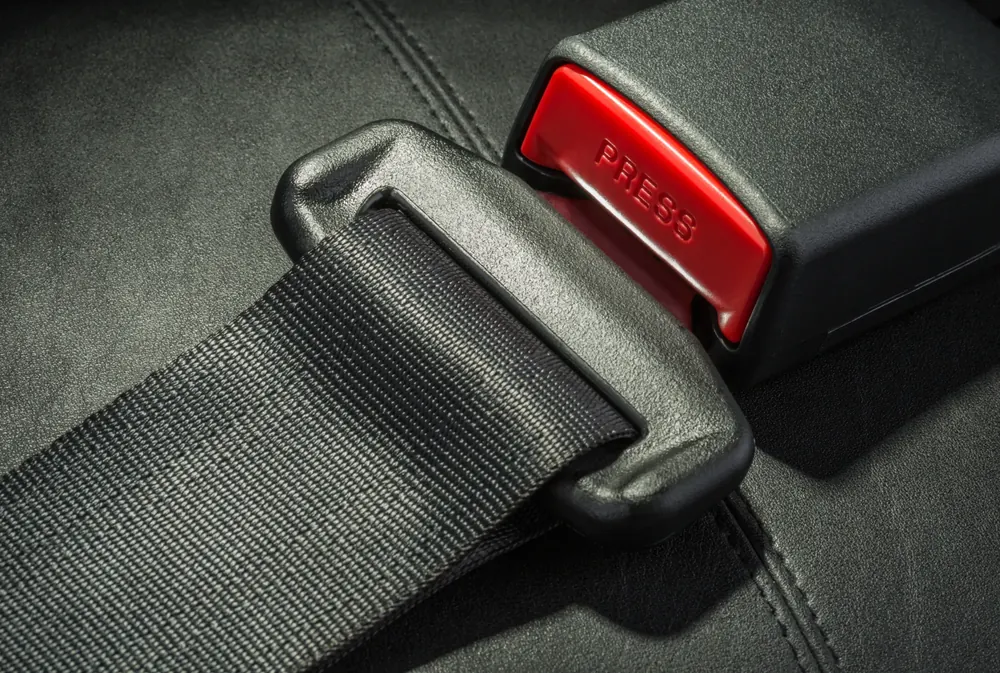 A seat belt assembly on a dark vehicle seat: webbing passing through the latch plate with the buckle receiver and its red release button alongside.