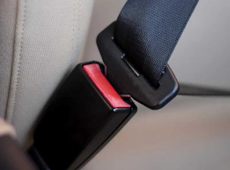 A seat belt buckle receiver and the webbing-mounted latch plate positioned just apart, against a pale fabric seat.